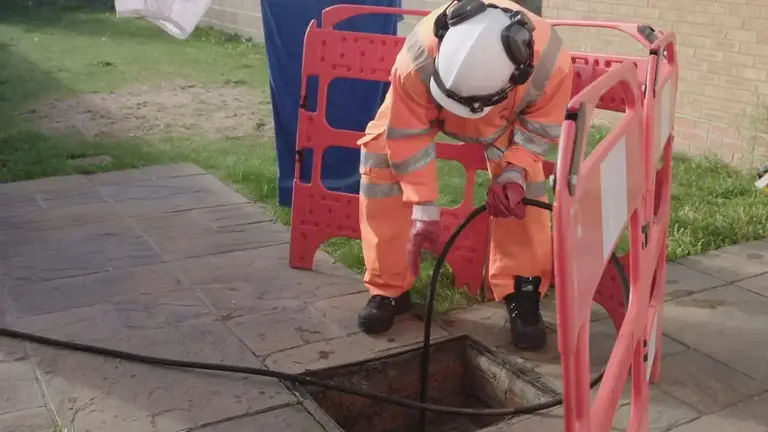 Drainage engineer feeding a hose into an inspection chamber behind safety barriers