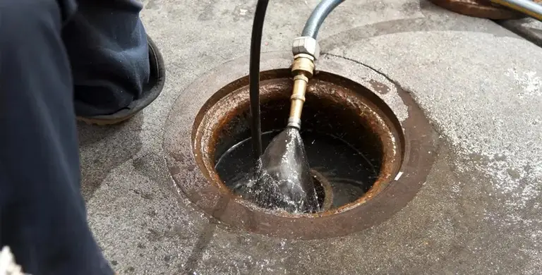 A jetting nozzle spraying into a round drain gully to break up a blockage.