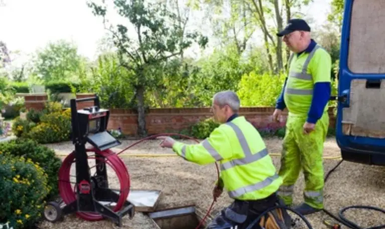 Two of our engineers running a CCTV camera into a drain from a cable reel, with the monitor beside them.